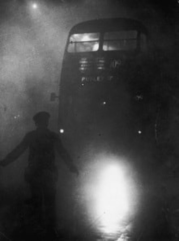 A bus barely visible in the Great Smog of London, December 1952, with a policeman guiding it by torchlight